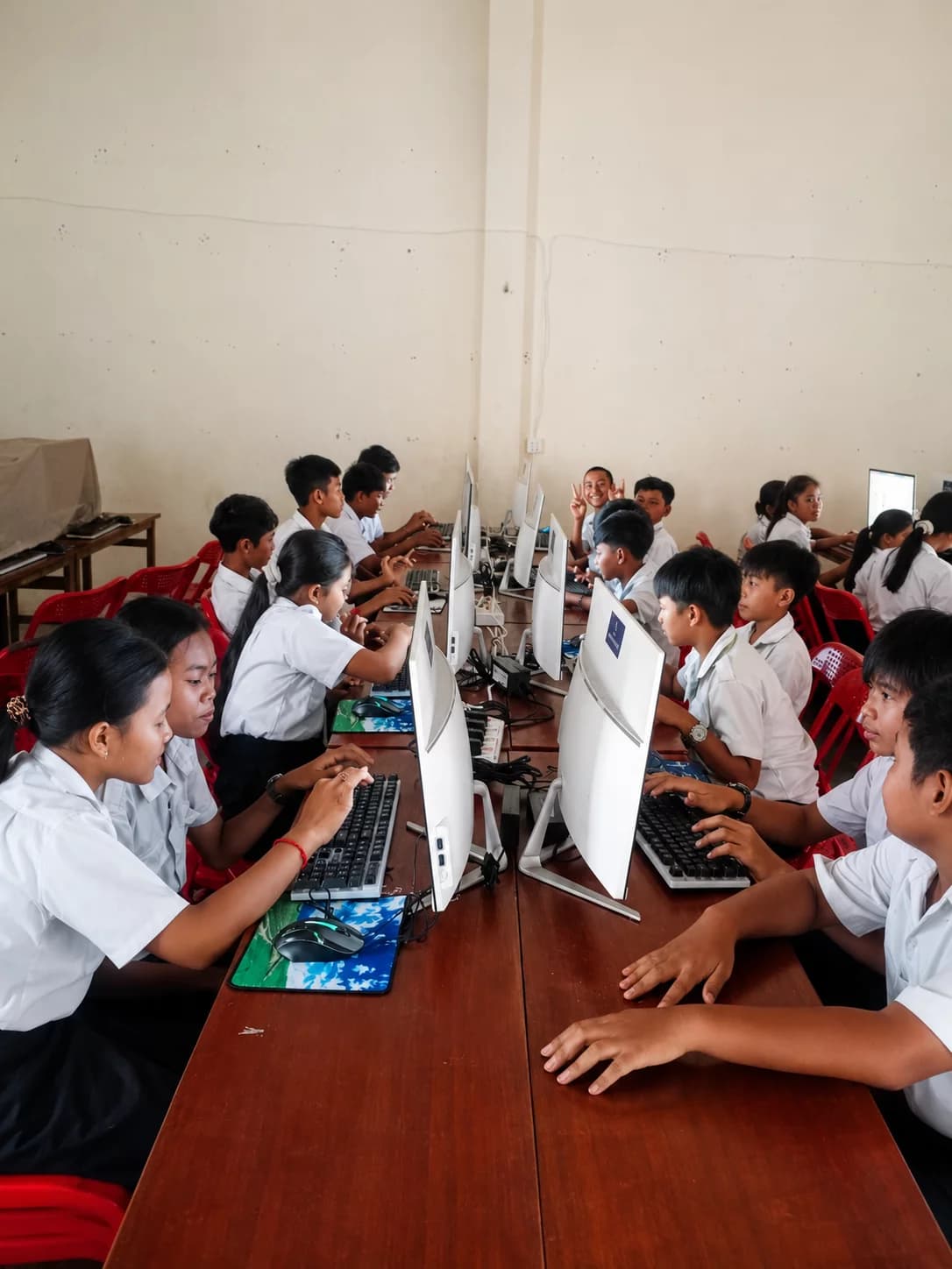 Students in school uniforms learning how to use desktop computers in a bright classroom computer lab